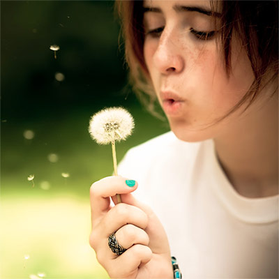 Teenage girl blowing a dandelion